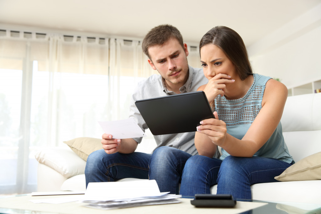 A worried couple looking at financial documents and a tablet at home
